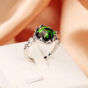 Close-up of a silver ring with a square green gemstone and white side stones on silk