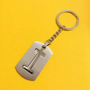 Detail of silver brushed metal keychain featuring a hollow cross cutout on yellow background