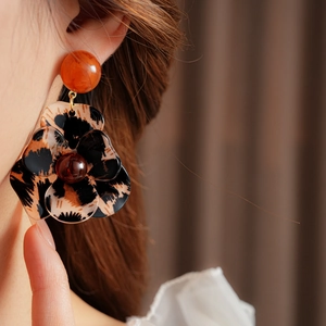 Close-up of resin leopard print flower earrings with orange studs on model's ear