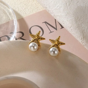 Chic golden starfish earrings with white round pearls displayed on elegant ceramic plate