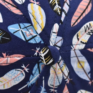 Macro detail of the top button and stitched seams on a colorful feather print baseball cap