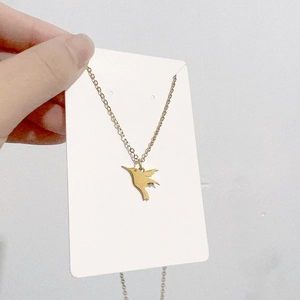 Vue rapprochée d'un collier pendentif colibri doré sur une carte blanche
