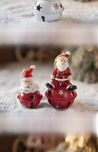 Detail of red metal Christmas bells with painted Santa Claus resin figurines on snow