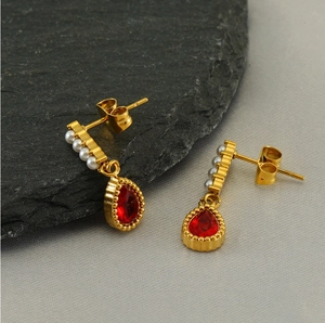 Detail of gold teardrop earrings featuring red zircon and small white pearls