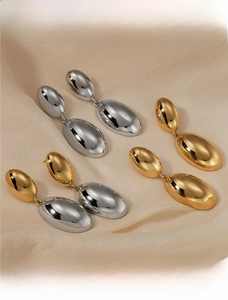Macro shot of three pairs of metallic water drop earrings on elegant beige silk fabric