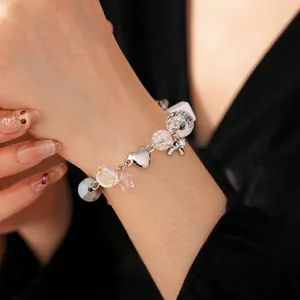 Silver beaded bracelet with star and bow charms worn by a model on a black background