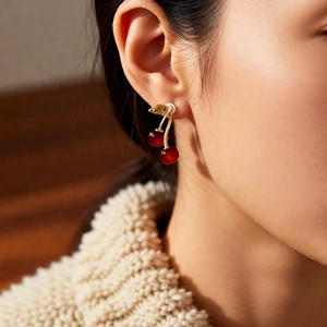 Detailed close-up of cherry pendant earrings featuring red spheres and gold leaf detail