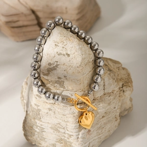 Macro detail of stainless steel bead bracelet with golden heart pendant and OT clasp