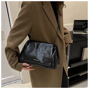 Detail of black glossy wrinkled texture bag with metal chain strap on a blazer