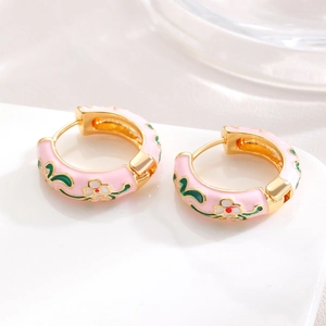 Macro detail of pink enamel floral earrings with gold trim on white ceramic tray