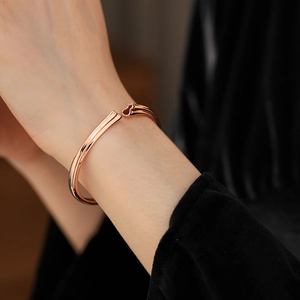 Close-up of a rose gold open bangle with a red agate gourd charm on a model's wrist