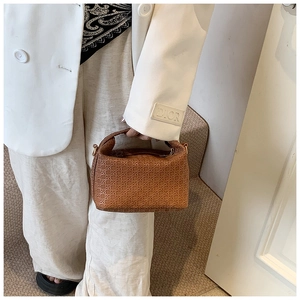 Close-up of brown woven texture mini pillow bag held by model in white suit