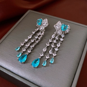 Detail of silver bow earrings featuring blue heart gems and long zircon tassels