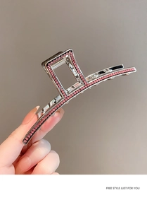 Detail of silver metal shark hair claw with pink rhinestones held by a hand