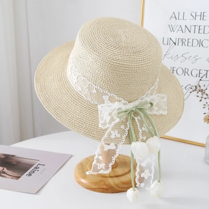 Detail of raffia sun hat featuring white lace trim and green bow with tulip pendants