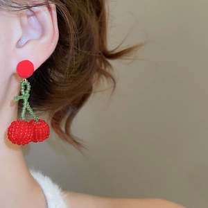 Macro shot of handmade cherry earrings featuring red beaded fruit and green leaf accents