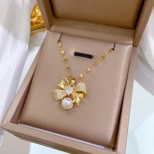 Close-up of golden bow necklace with heart zircon and pearl in a velvet box