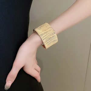 Close-up of golden wide cuff bracelet featuring elegant linear brushed metal texture