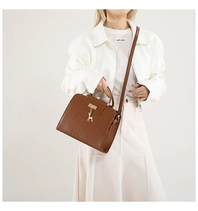 Detail of brown crocodile pattern handbag with golden deer pendant and metal handles