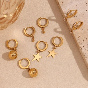 Detail of 18K gold-plated earrings with star pendants and zircons on a stone background