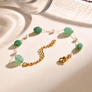 Detailed close-up of gold-plated bracelet with green stones and elegant white pearls