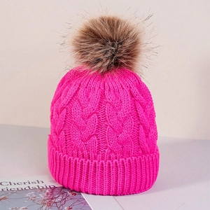 Detail of rose red cable knit winter beanie with a large faux fur pompom on top