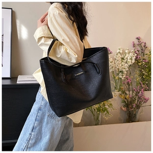 Macro shot of textured black faux leather tote bag with elegant gold brand plaque
