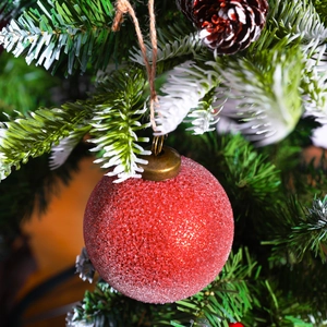 Sparkly red glitter Christmas ball ornament hanging on a pine tree with a jute rope