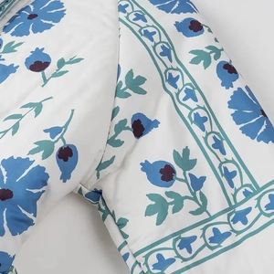 Detail of white quilted jacket featuring blue floral print and intricate stitching seams