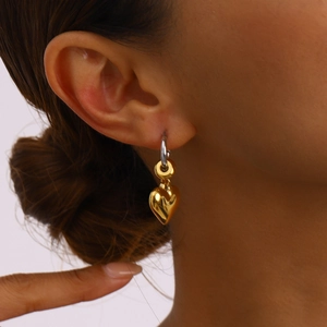 Close-up of heart charm earrings in gold and silver finish on a model's ear