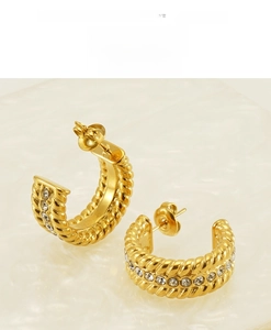 Macro view of gold-plated twisted U-shape hoop earrings with sparkling rhinestones