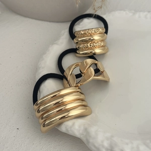 Three gold metal hair ties with chain and wave textures on a white ceramic plate