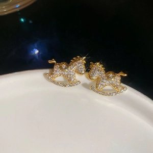 Macro shot of sparkling zircon pony earrings on white porcelain tray with gold accents
