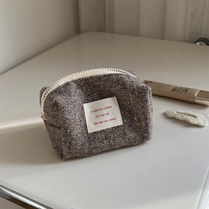 Macro shot of herringbone tweed makeup bag with white resin zipper on creamy table