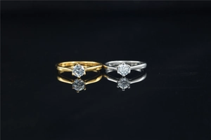 Close-up of gold and silver minimalist six-prong moissanite rings on black mirror