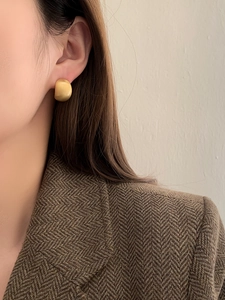 Close-up of minimalist matte gold curved stud earring worn on model with textured suit