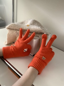 Detail of orange knit gloves with bear embroidery showing soft texture and pattern