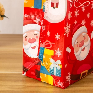 Red Christmas non-woven gift bag featuring Santa Claus and snowflakes on a wooden table