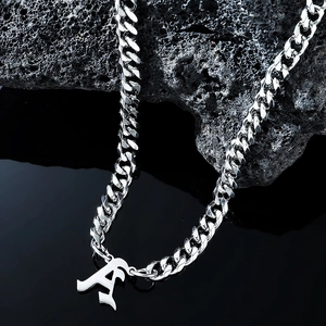 Macro detail of silver Gothic letter A pendant on a Cuban link chain over volcanic stone