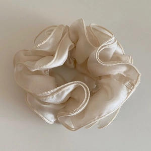Close-up of cream white silk scrunchie with soft pleated texture and elegant satin sheen