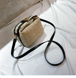 Close-up of beige woven straw crossbody bag featuring black leather trim and gold hardware