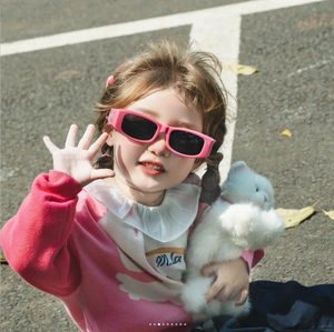 Detail of pink square frame children's sunglasses with dark lenses on a child outdoor