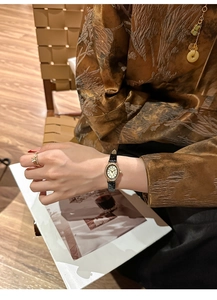 Close-up of a vintage oval ladies watch with gold case and black leather strap on wrist