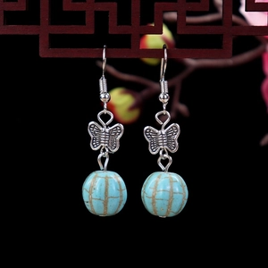 Detail of retro butterfly earring with blue turquoise bead hanging on wooden window