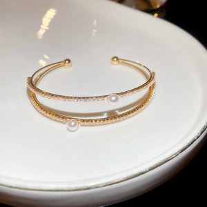 Detail of double-layer gold bangle featuring sparkling zircons and white pearls