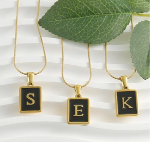 Detailed shot of gold snake bone necklaces with black square initial pendants S, E, and K