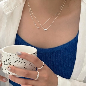 Detail of layered silver heart necklace and natural freshwater pearl ring on a model