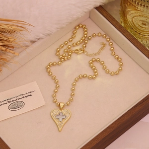Detail of a gold heart pendant with zircon pavé and clover cross on a ball chain