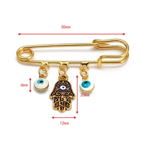 Detailed view of gold Hamsa Hand and Evil Eye charms on a 50mm safety pin brooch