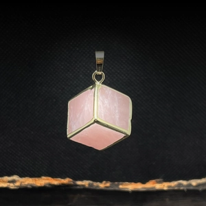 Close-up of pink crystal cube pendant with gold plated edges on black textured background